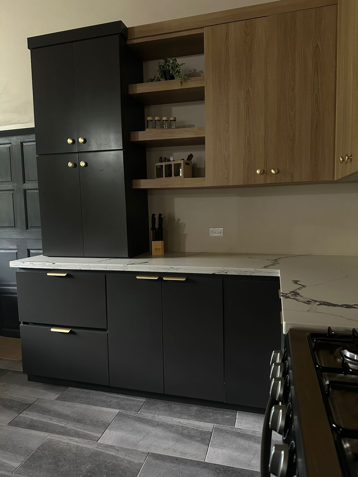 Matte black cabinetry, warm oak and marble — a working heart.