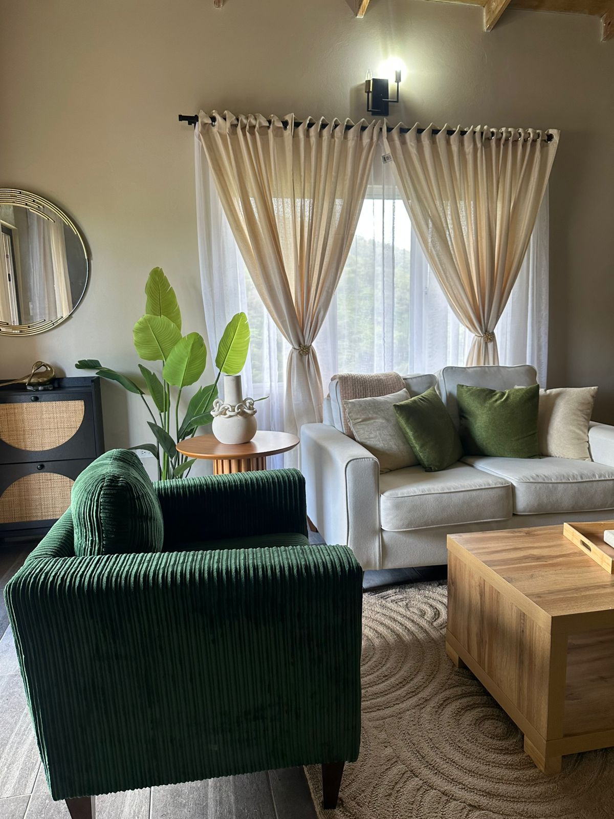 Emerald corduroy armchair, linen sofa and layered sheers in a light-filled lounge.