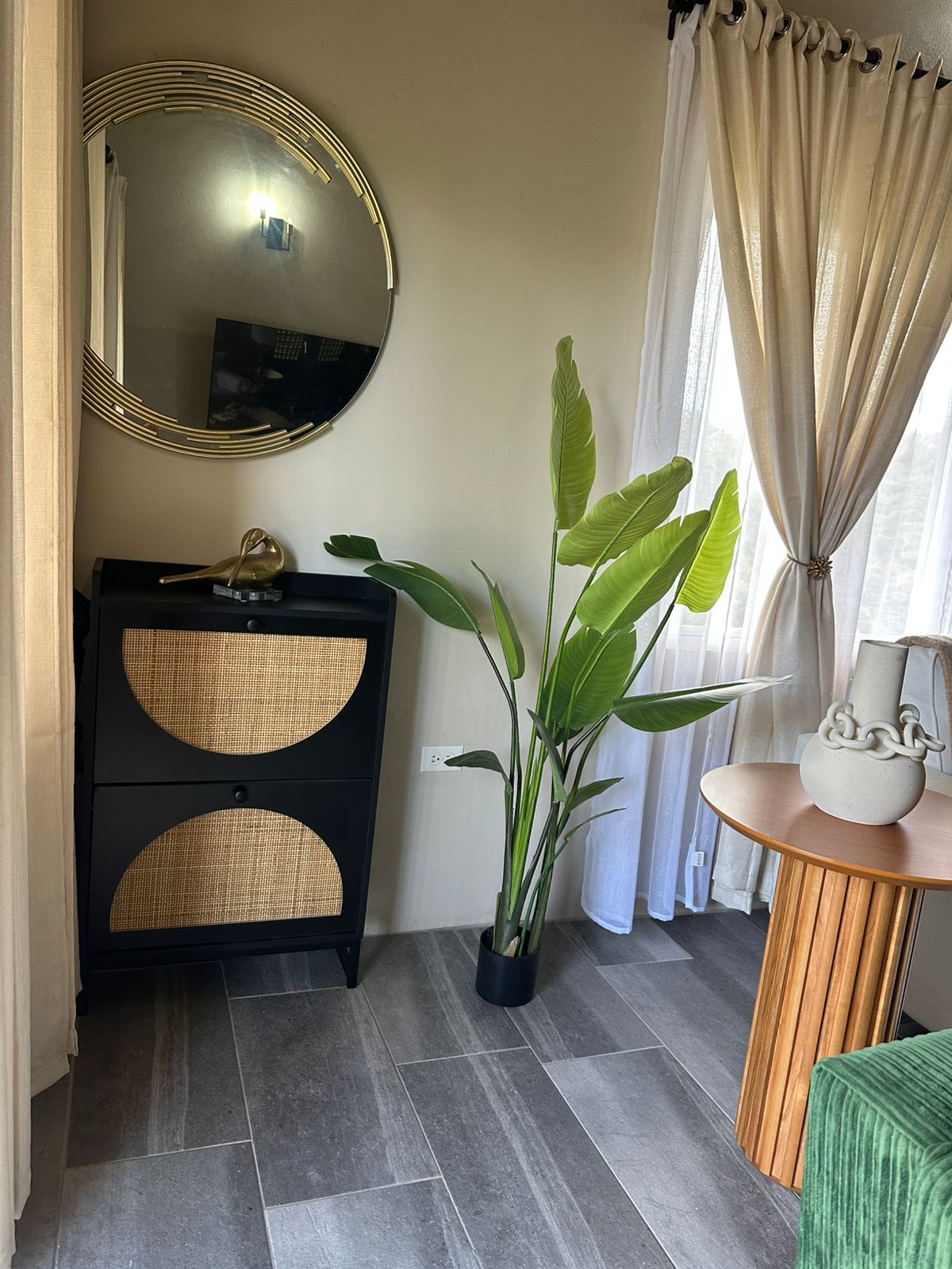 Rattan cabinet, brass round mirror and sculptural greenery in a quiet entry.