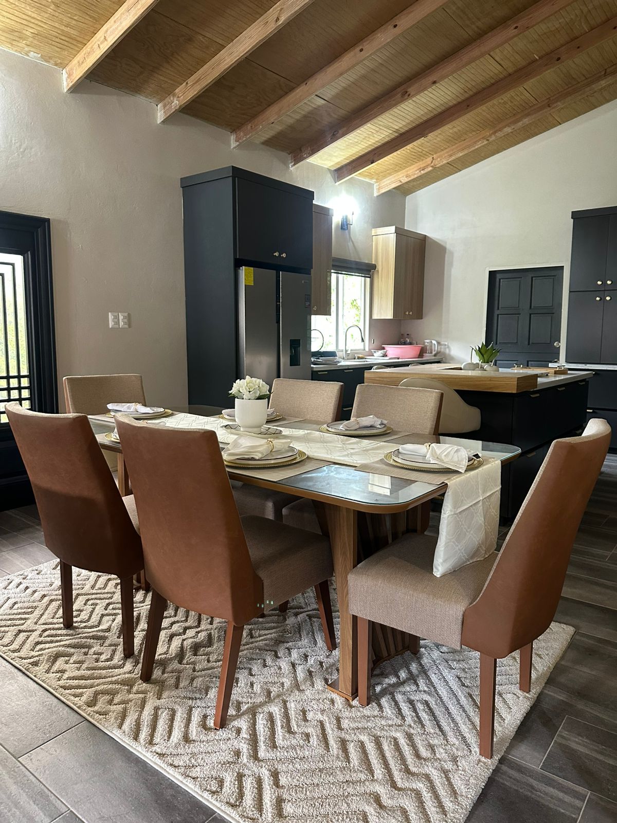 Open-plan dining with exposed beams, tan leather chairs and a matte black kitchen.