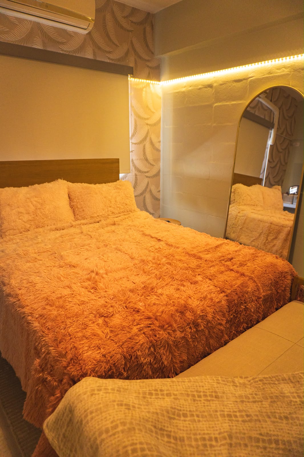 Warm-lit bedroom with plush bedding, leaf wallpaper and an arched brass mirror.
