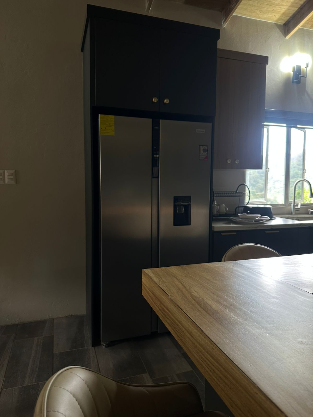 Custom black tower cabinetry framing the fridge under exposed wood beams.