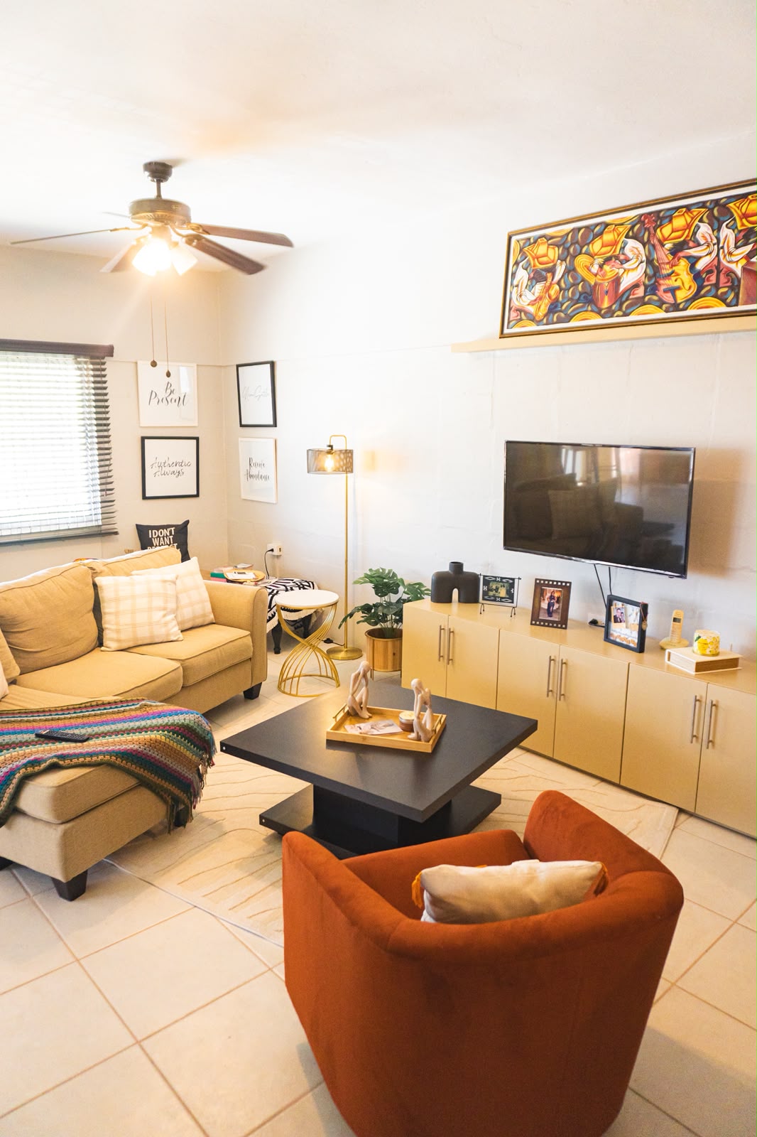Living room with a rust velvet armchair, gold accents and vibrant statement art.